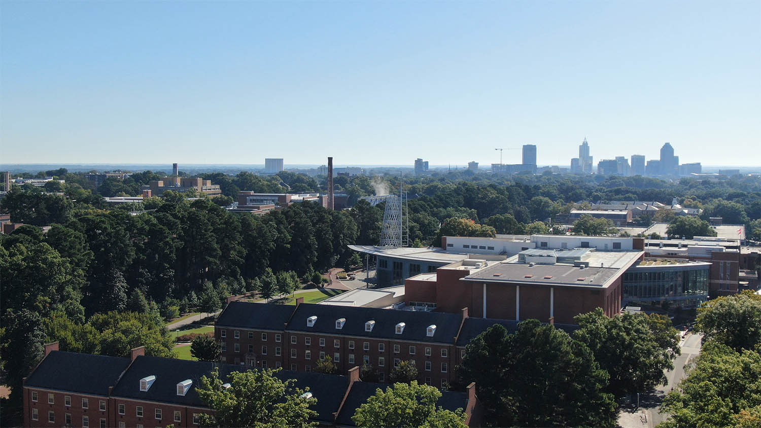 An aerial view of brick buildings and Talley Student Union, with downtown Raleigh in the background
