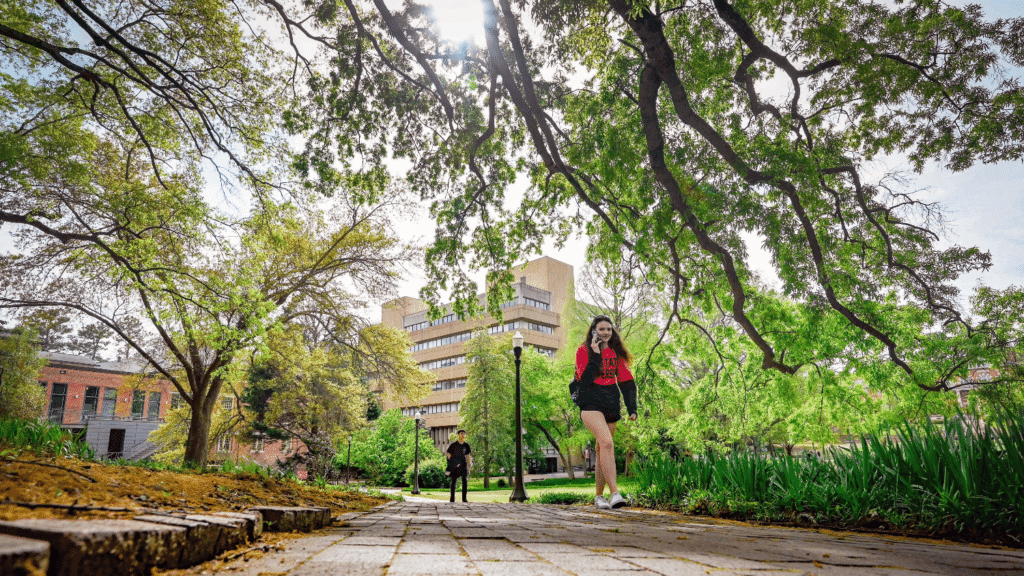 Students stroll through the Court of North Carolina on a warm spring afternoon with pollen falling in the foreground and Poe Hall in the background.