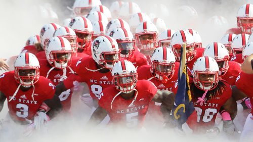 The NC State football team emerges from smoke