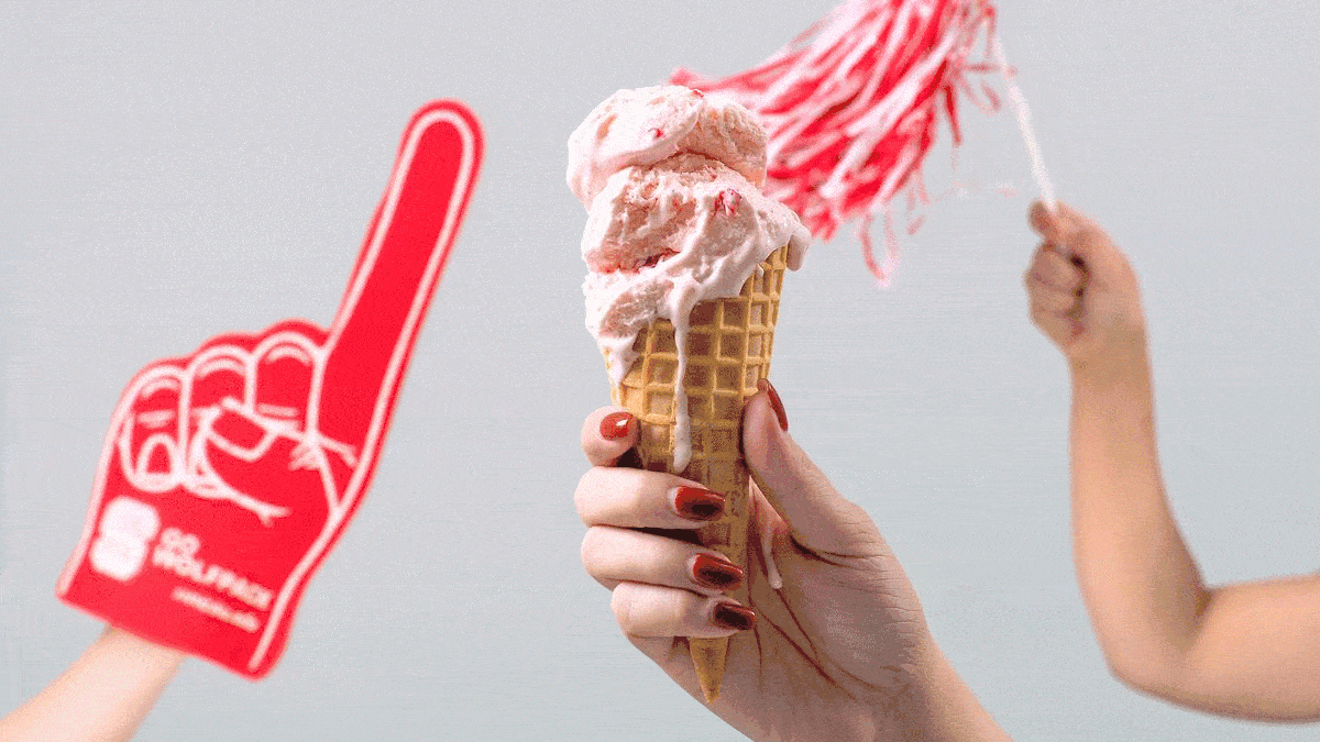 People wave NC State pom-poms and a foam finger behind a cone of Howling Cow ice cream