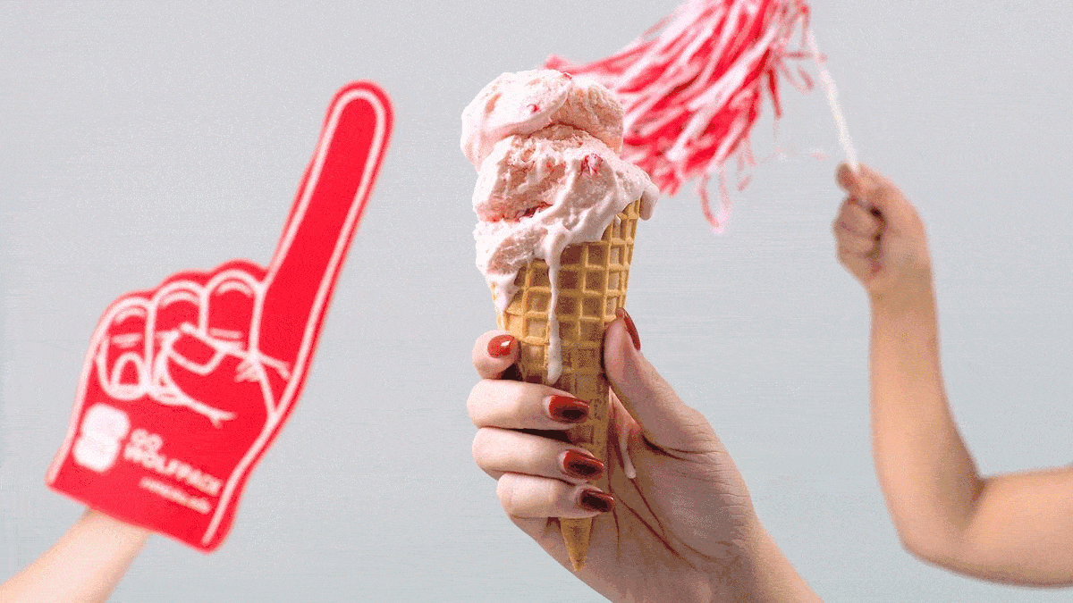 People wave NC State pom-poms and a foam finger behind a cone of Howling Cow ice cream