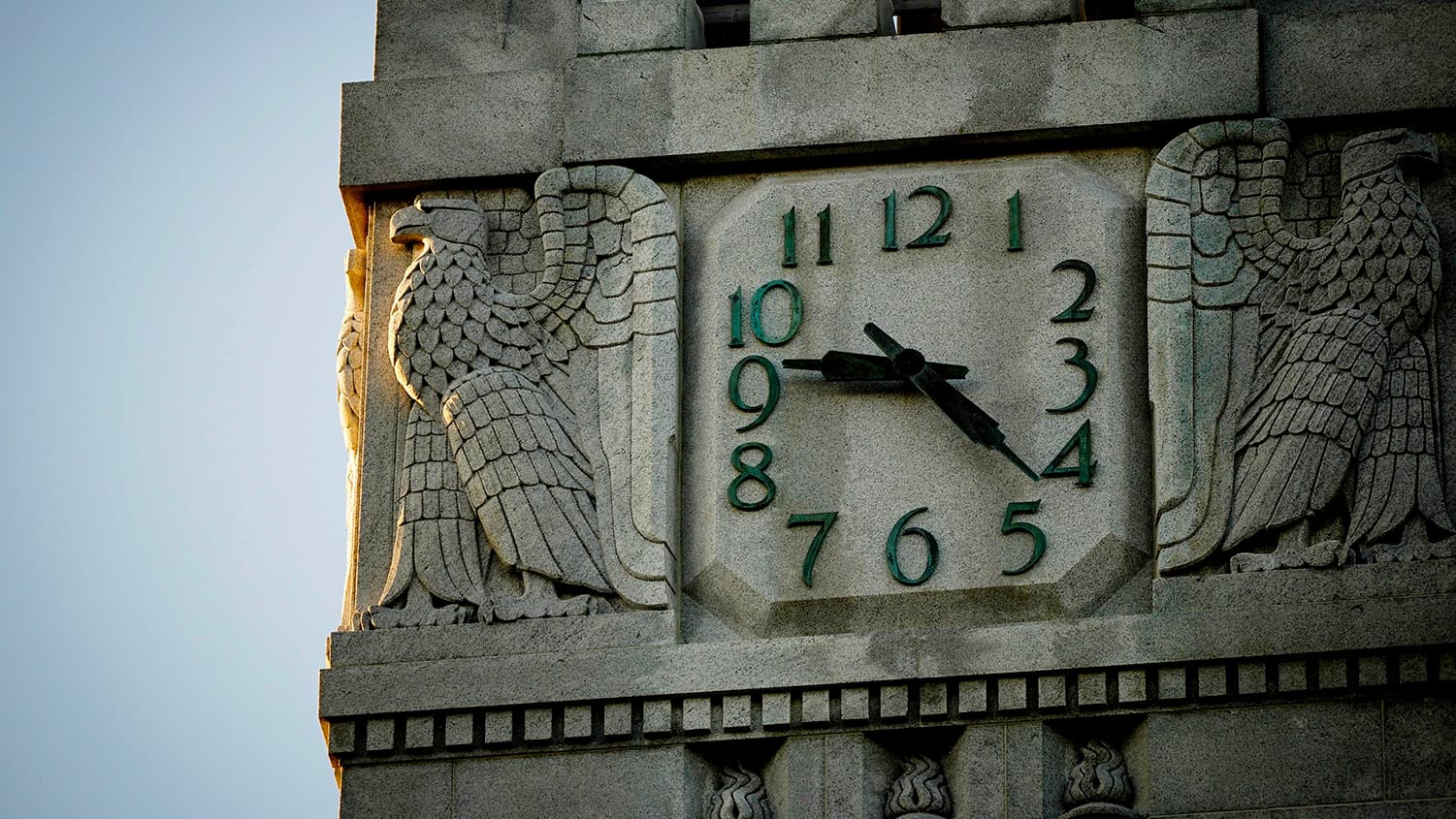 A clockface sitting high up on the Memorial Belltower, surrounded by two eagles.