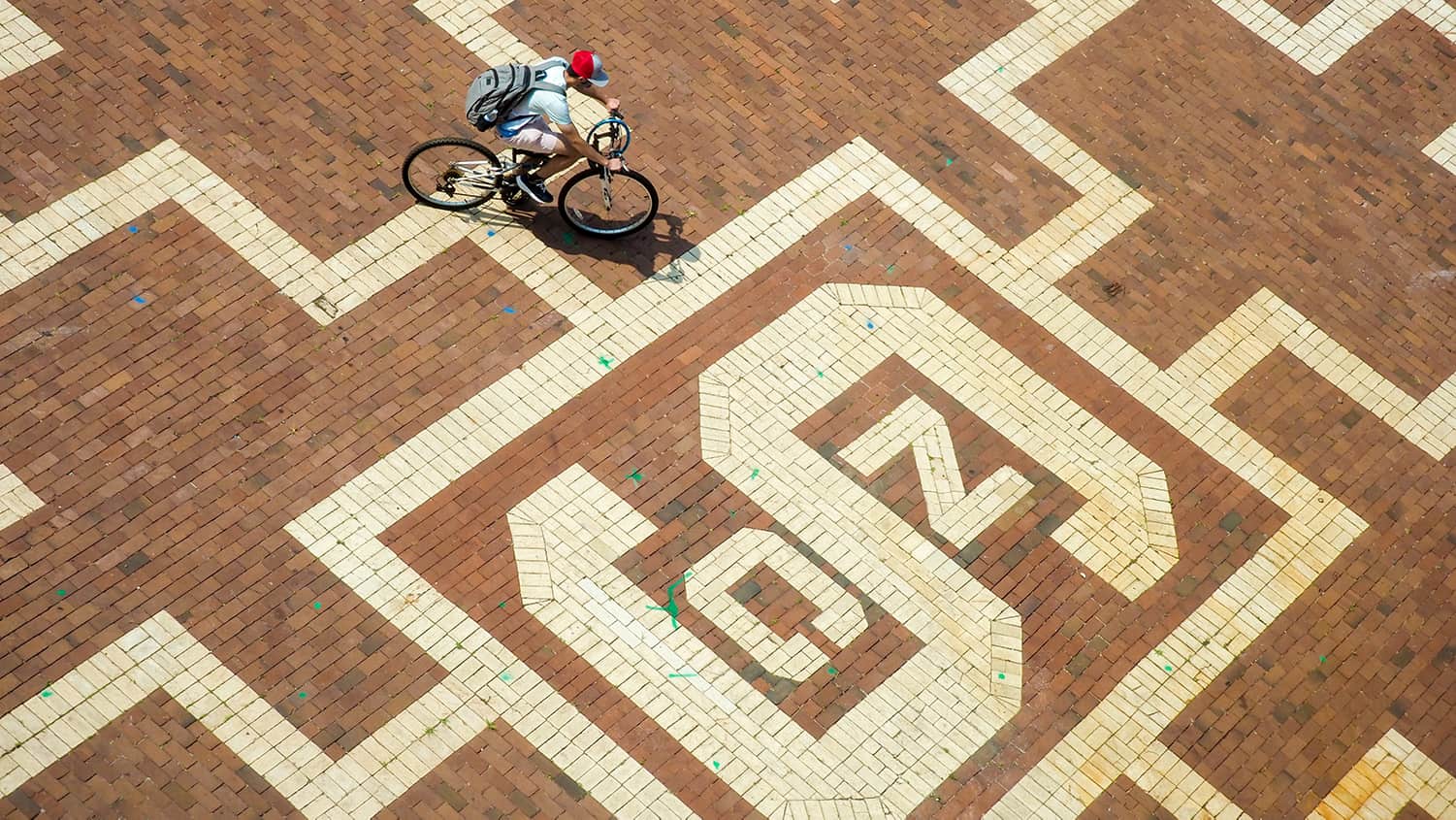An overhead view of a student riding a bike across the patterned Brickyard.