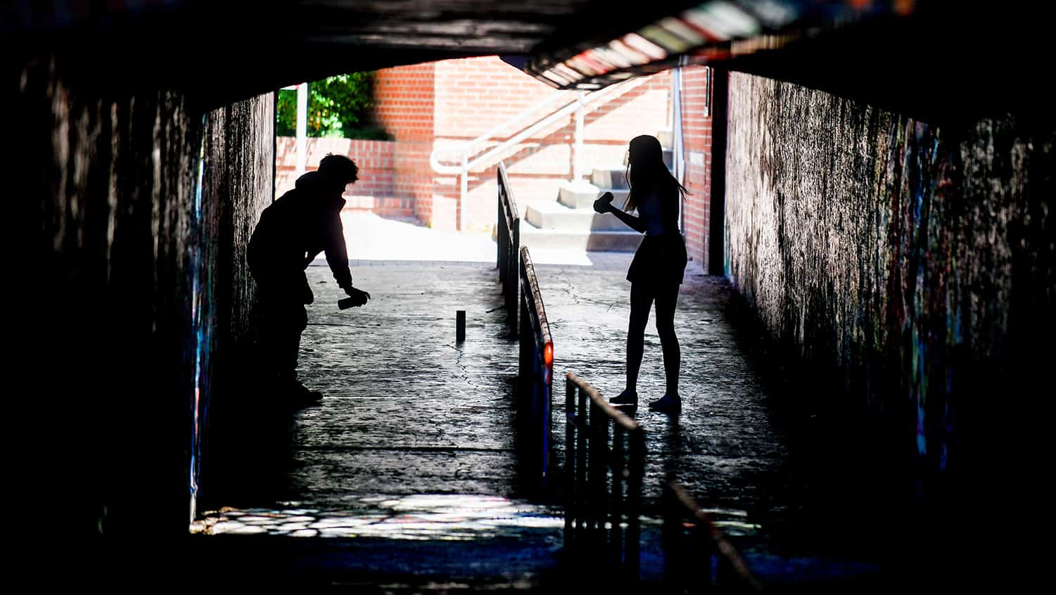 Two silhouetted students spray paint the Free Expression Tunnel.