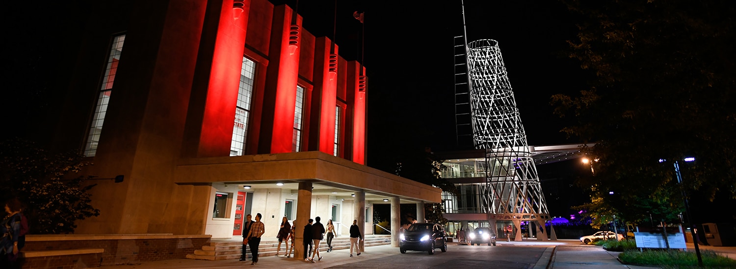 The exterior of Reynolds Coliseum at night, lit in red.