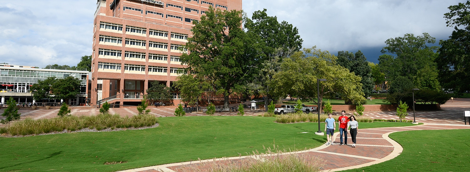 Three students walk across a brick pathway in University Plaza.