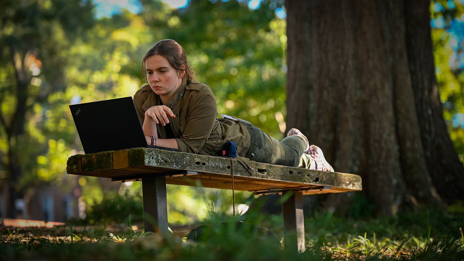 A student studies outdoors on a bench on a fall day.