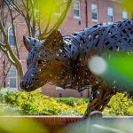 A copper wolf peeks from behind sprouting green leaves.