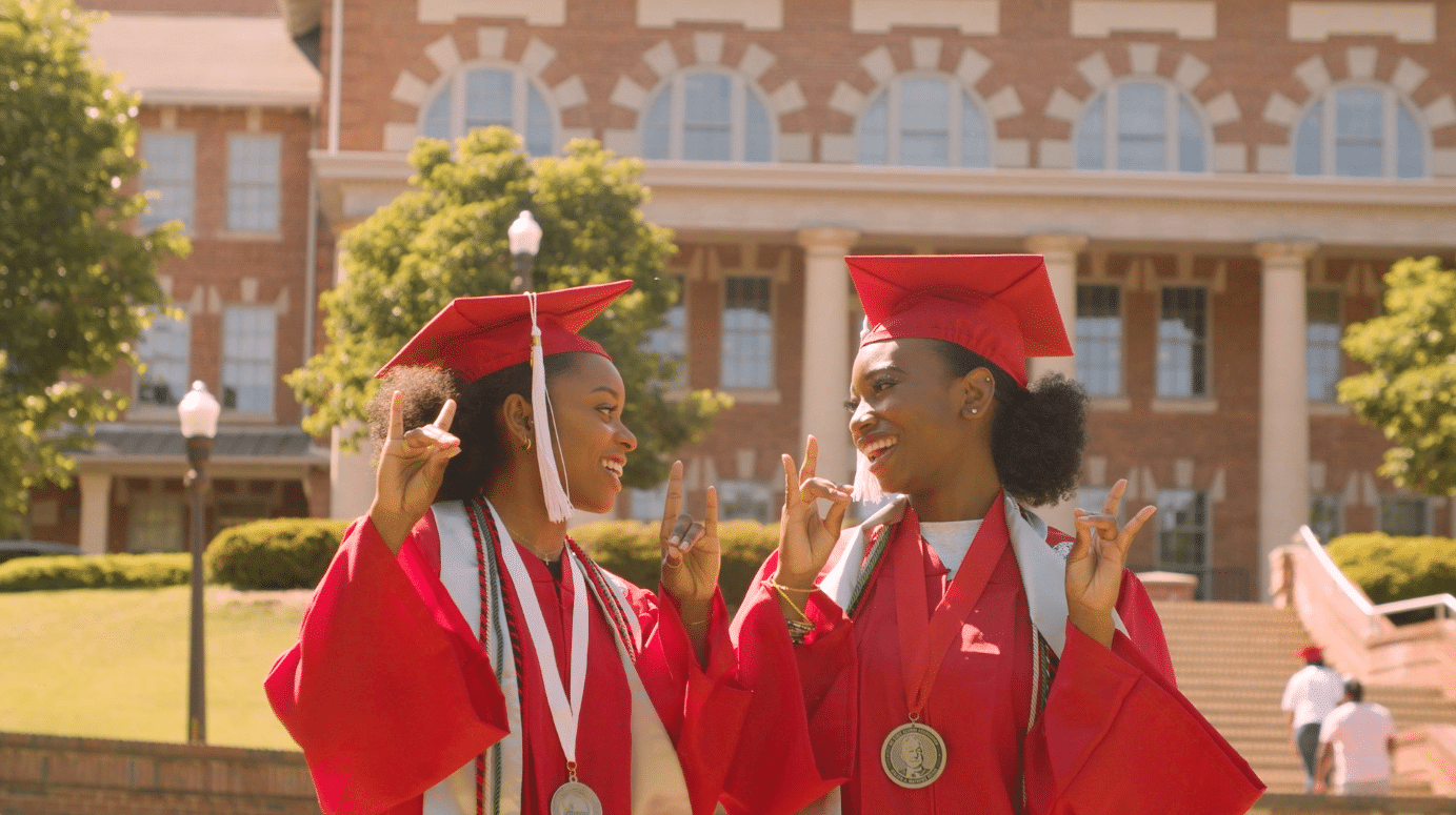 Niambé James and Kourtni Curry hold up wolfies in the Court of North Carolina while wearing red graduation robes.