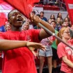 Students wearing red NC State t-shirts twirl flags at convocation.
