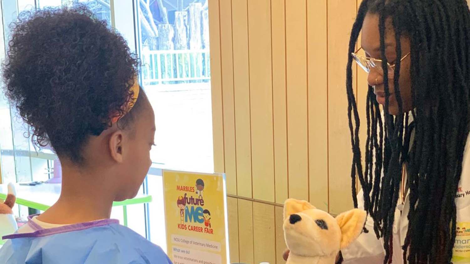 A veterinarian speaks with a young girl while holding a stuffed animal.