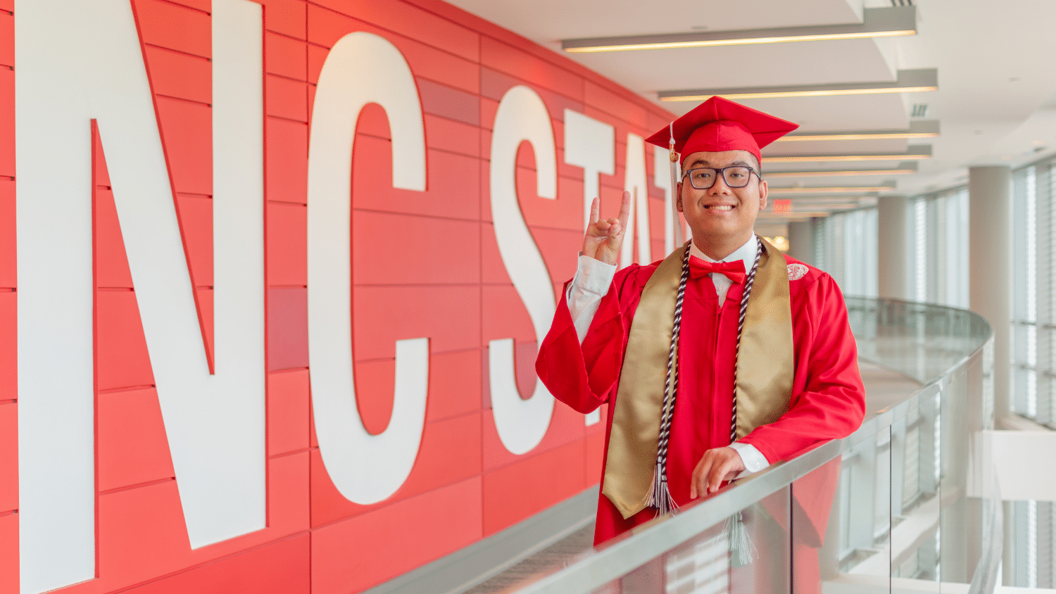 Graduating education student Don Bui stands in front of the NC State sign in Talley Student Union.