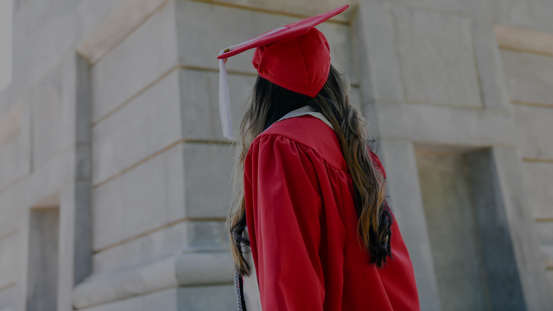 A student in red graduation robes turns around to look up at the Belltower.