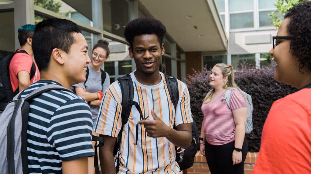 A group of students chat outside of Bragaw Hall.