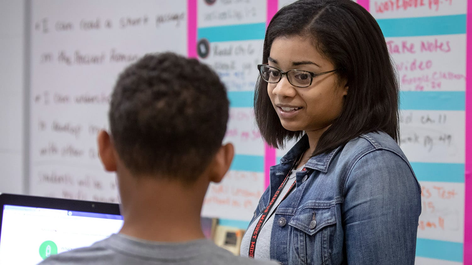 A student teacher talks to a young student in a classroom.