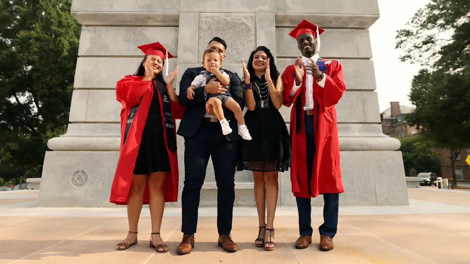 A family celebrates two new graduates while standing at the base of the Belltower.