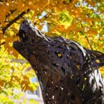 A copper wolf statue surrounded by vibrant yellow leaves.