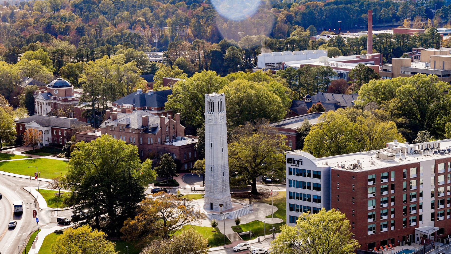 An aerial view of NC State's campus, showing the Belltower, Holladay Hall and the State College smokestack.