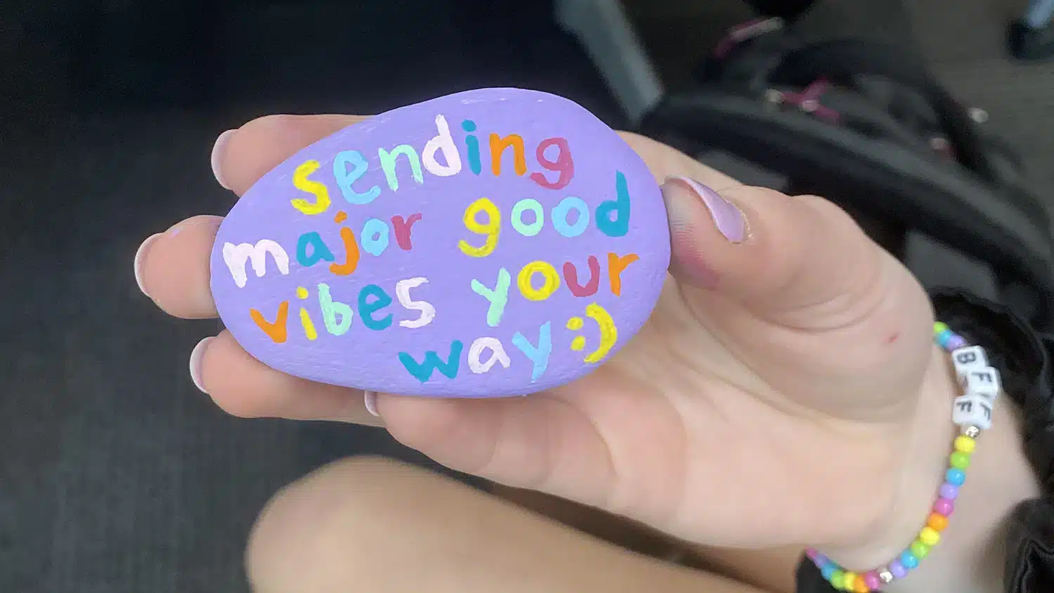 Student holding rock painted purple that reads, "sending major good vibes your way".