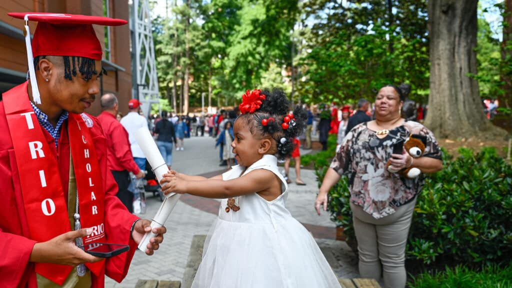 A graduating student of NC State shows his diploma to a young girl.