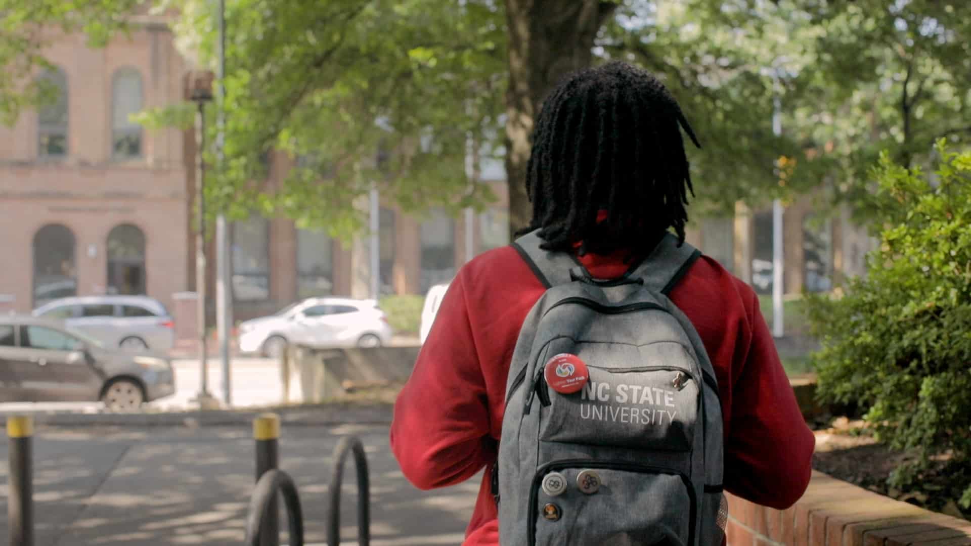 A student walks across campus with a backpack that has a "Lighten Your Pack" pin.