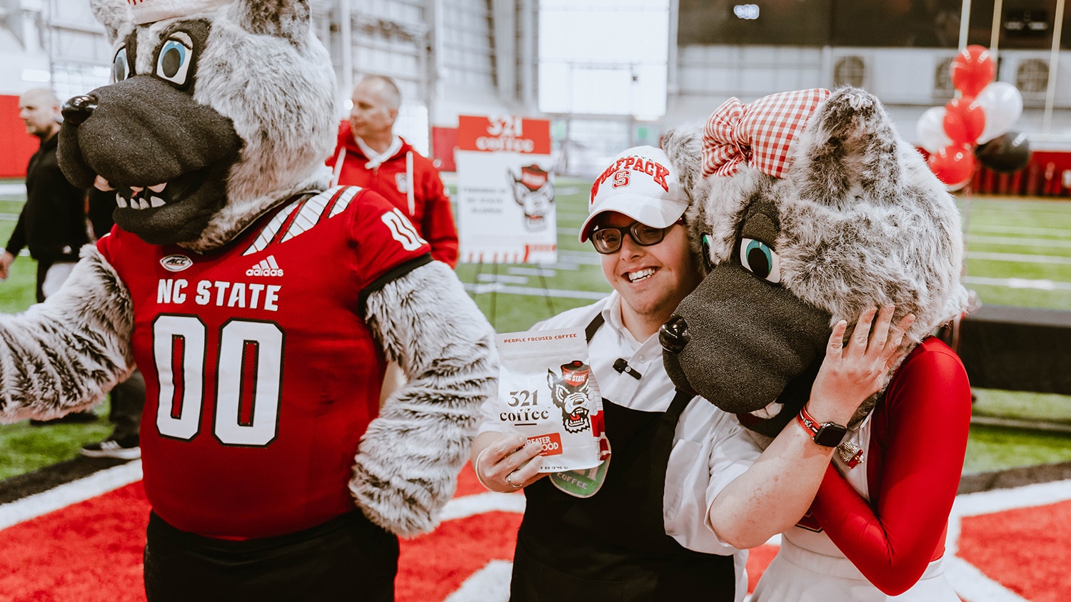 Sam, a 321 Coffee employee, hugs Ms. Wuf while holding a bag of the company's new NC State co-branded Greater Good coffee.