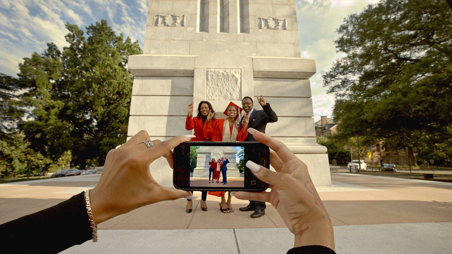 A proud NC State graduate has her picture taken with her family in front of the Memorial Belltower.