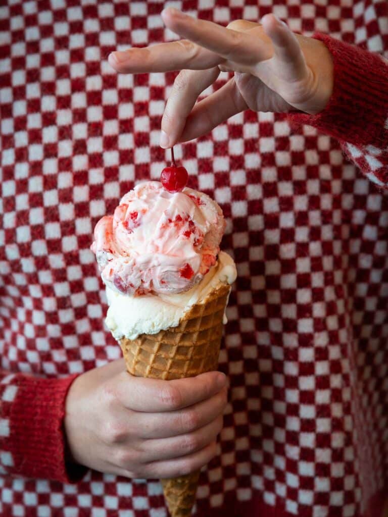 A Howling Cow ice cream cone held up against a red checkered background.
