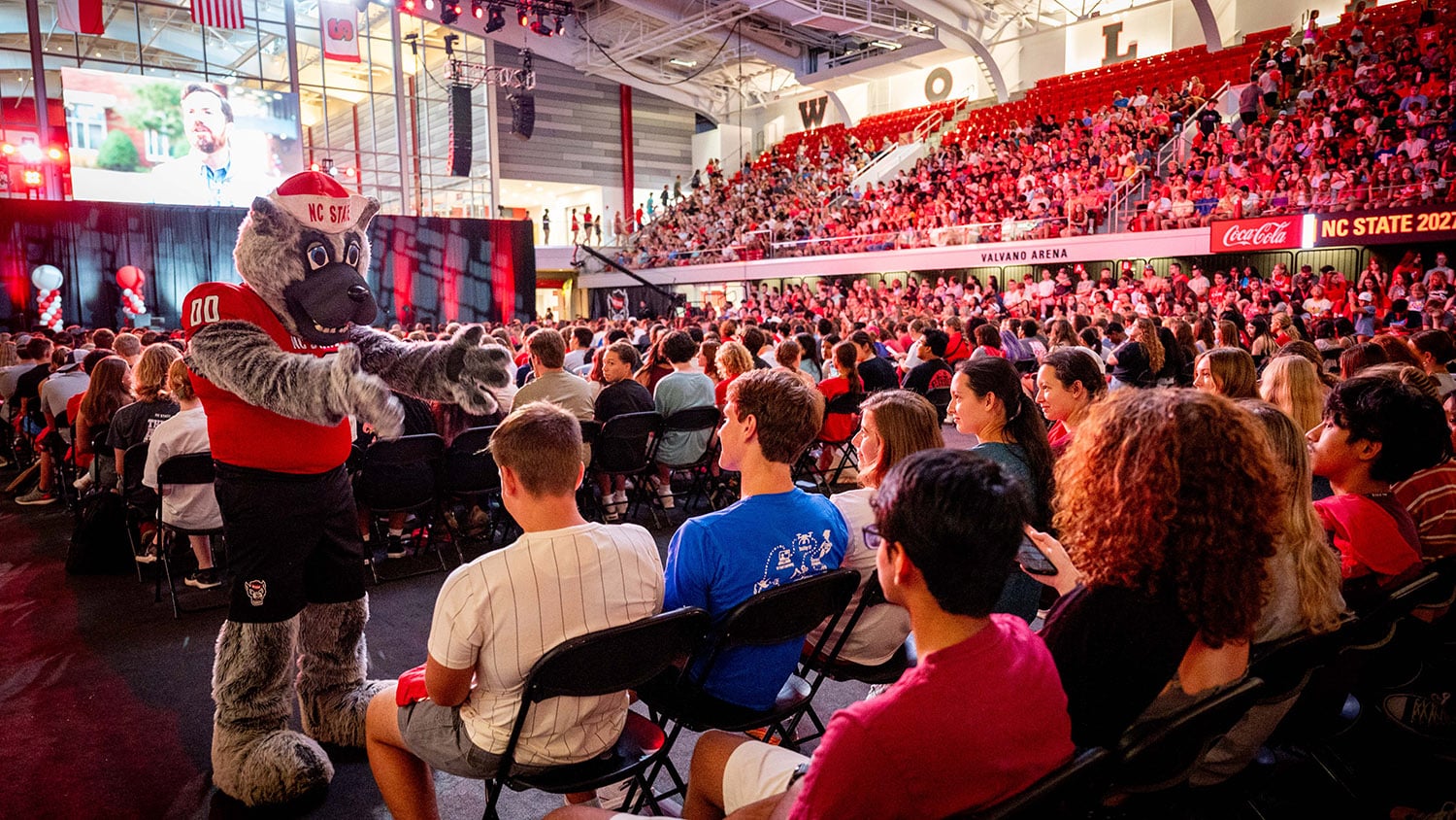 Mr. Wuf gestures toward a group of seated students during New Student Convocation in Reynolds Coliseum.