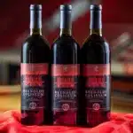 Three bottles of NC State wine on a red tablecloth in Reynolds Coliseum.