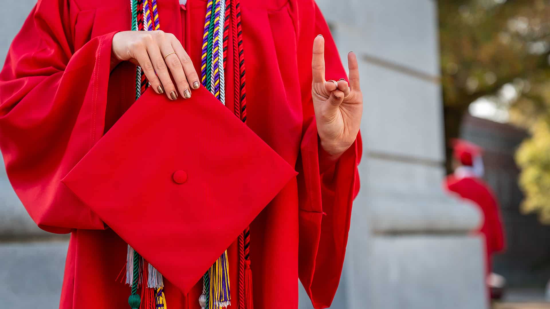 A student holds up wolfies and a red graduation cap.