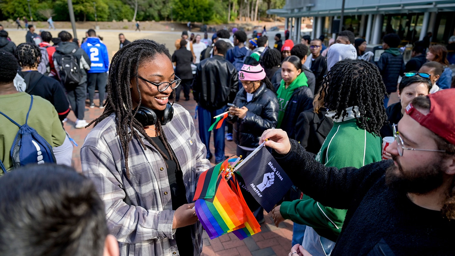 A student hands out flags to other students in a large crowd gathered on Stafford Commons for the March Like Martin event on Martin Luther King Jr. Day, 2024. The flag the student is selecting reads "Black Lives Matter."
