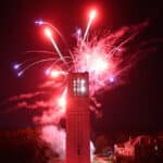NC State's Belltower surrounded by red fireworks.