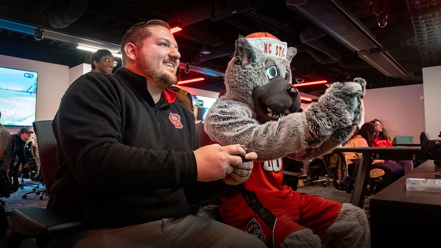 NC State Esports Program Director Cody Elsen enjoys a friendly gaming session with Mr. Wuf in the new NC State Gaming and Esports Lab.