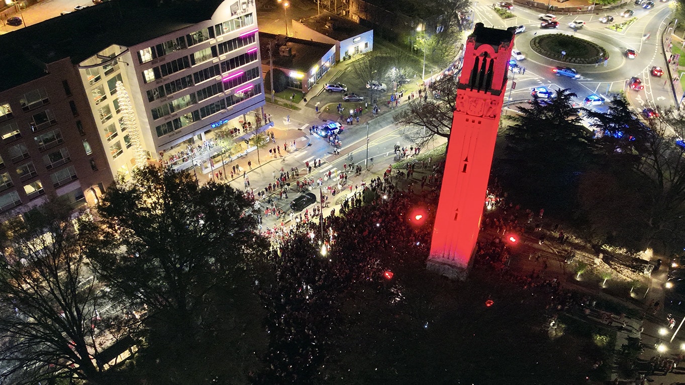 An aerial shot of the NC State Belltower lit red with a crowd around it after the Final Four of the NCAA men's basketball tournament.