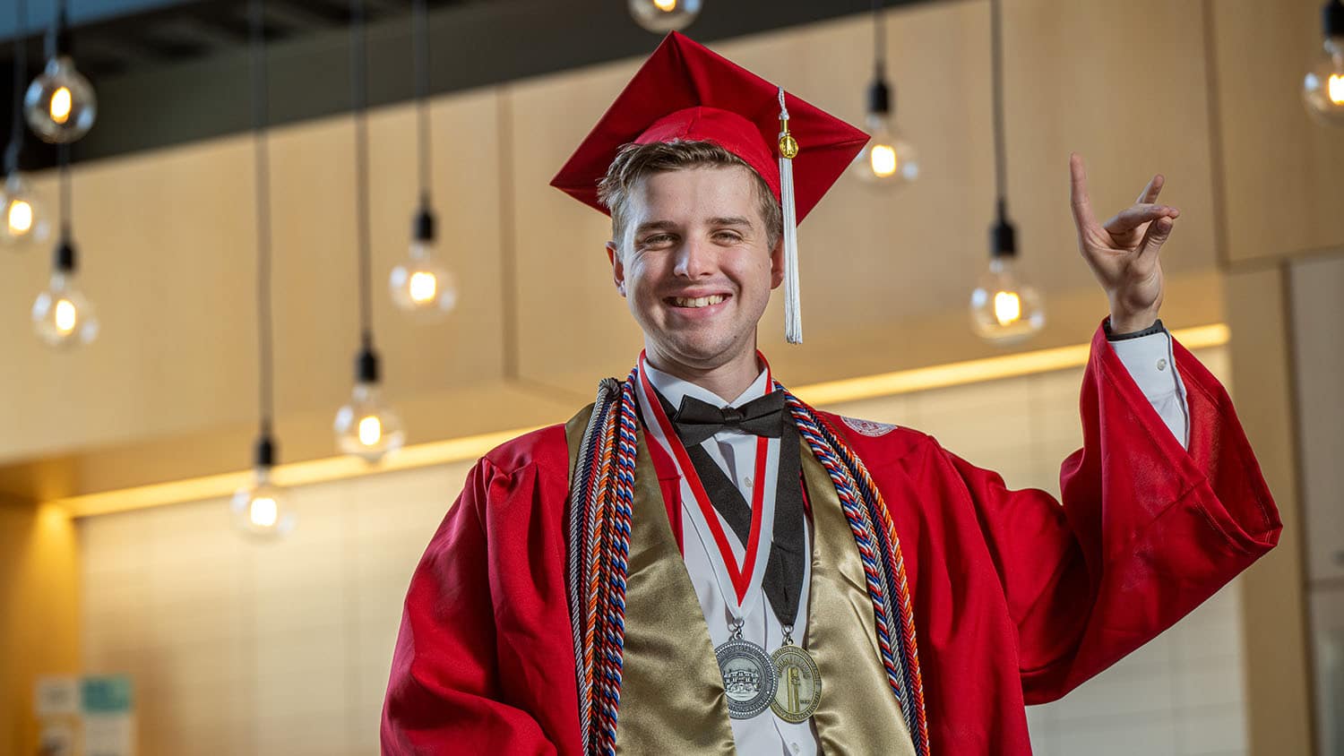 Shaun Deardorff, a College of Engineering student graduating this spring, stands in his red cap and gown.