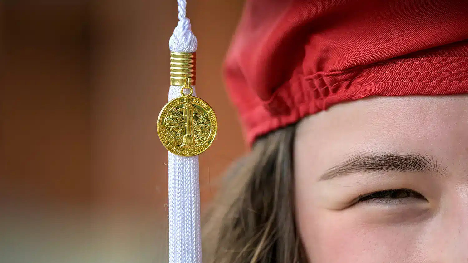 A student wearing a red graduation cap looks into the future.
