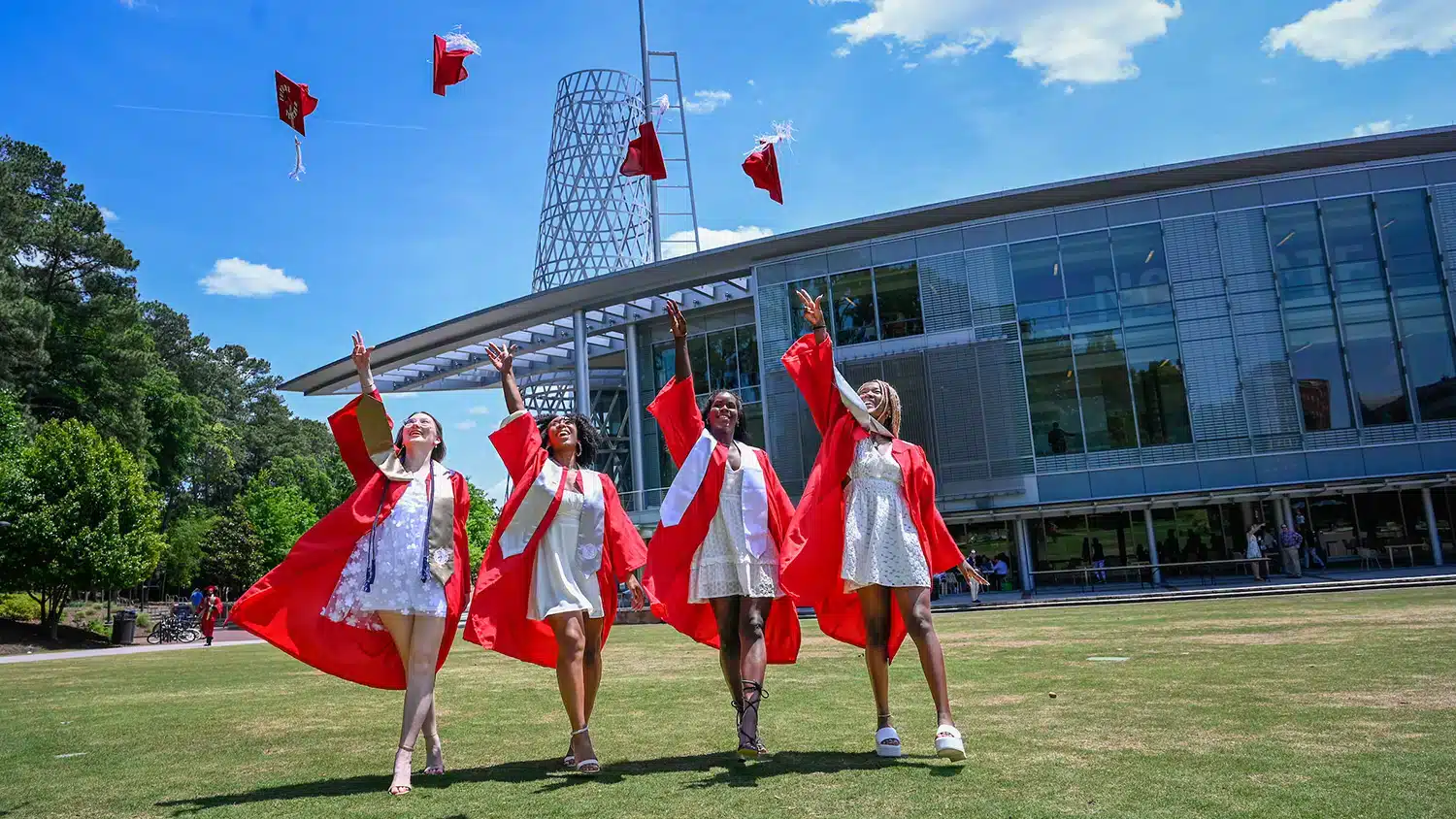 Four students throw their red graduation caps in the air on Stafford Commons.