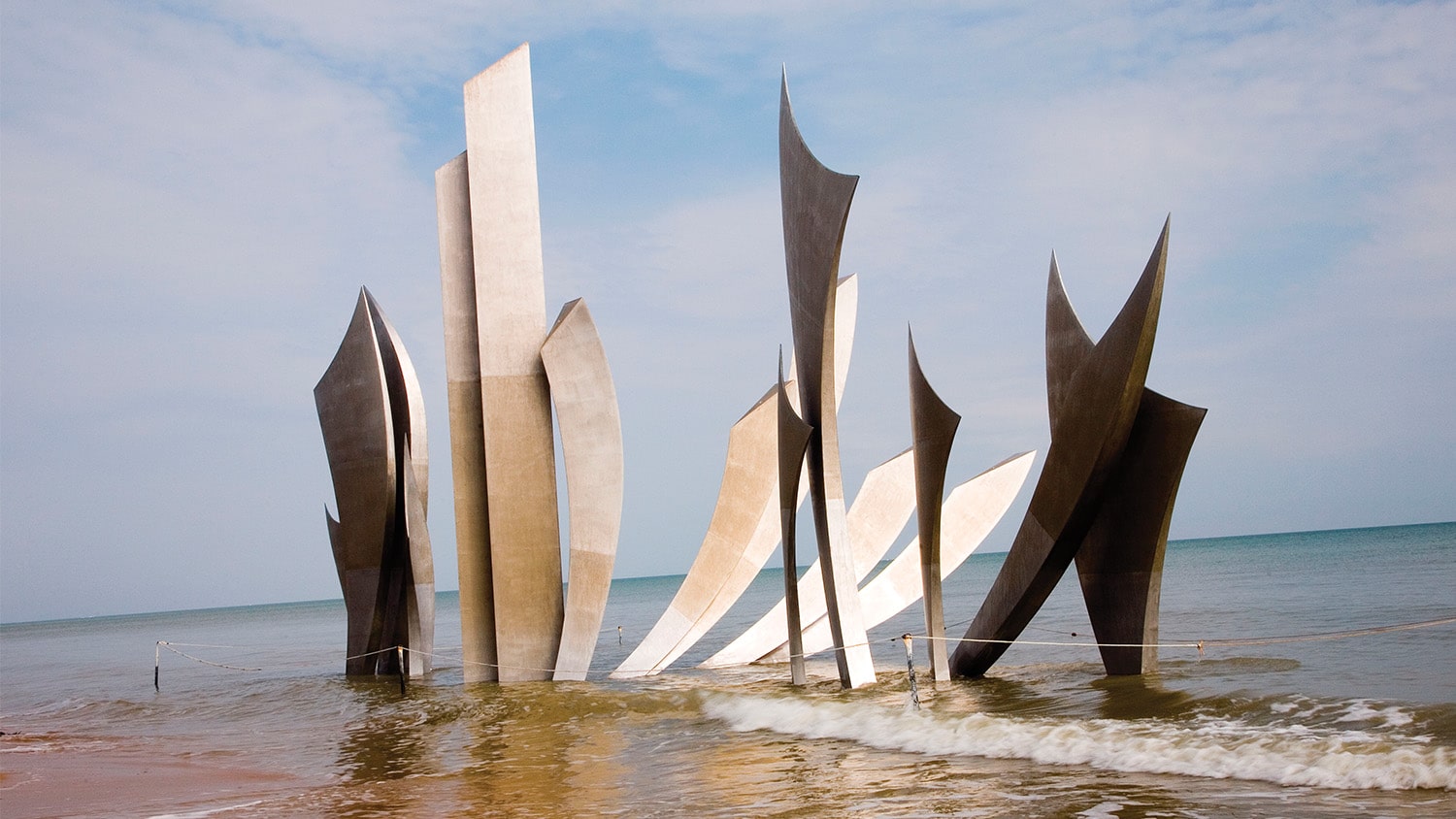 On Omaha Beach’s shore, waves come upon Les Braves, a monument commemorating Allied troops who landed on June 6, 1944. Photograph © Tim Wright / Alamy stock photo