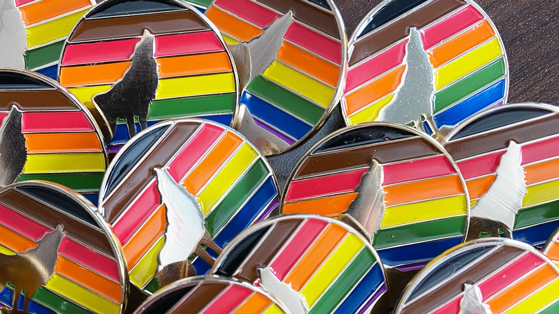 A closeup of a collection of rainbow pins with a howling wolf featured on them.
