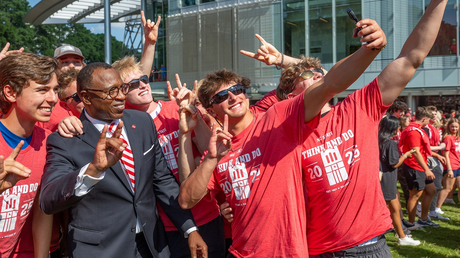 A group of students in red NC&#160;State T-shirts gathers around Chancellor Kevin Howell to take a selfie.